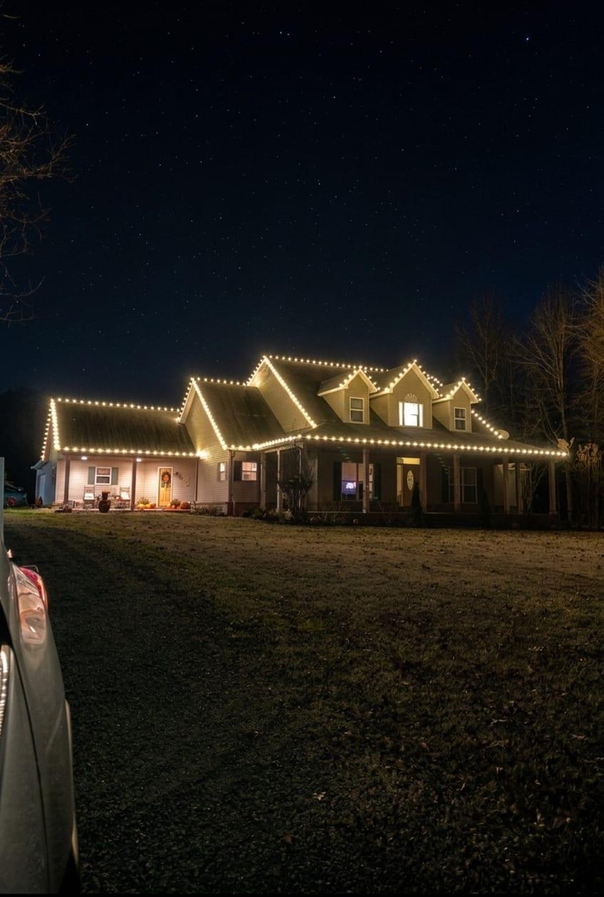 Farmhouse under a starry night sky, outlined in warm white C9 bulbs along every roof peak, dormer, and porch eave