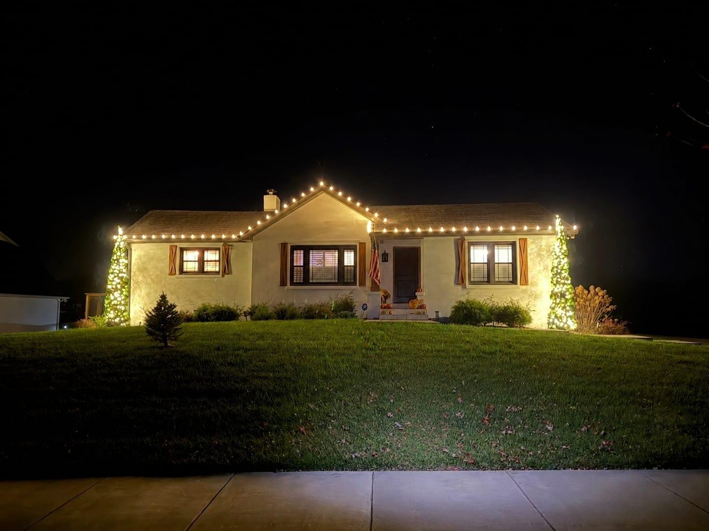 Ranch home at night with a warm white roofline and two cone-shaped lit trees framing the front porch