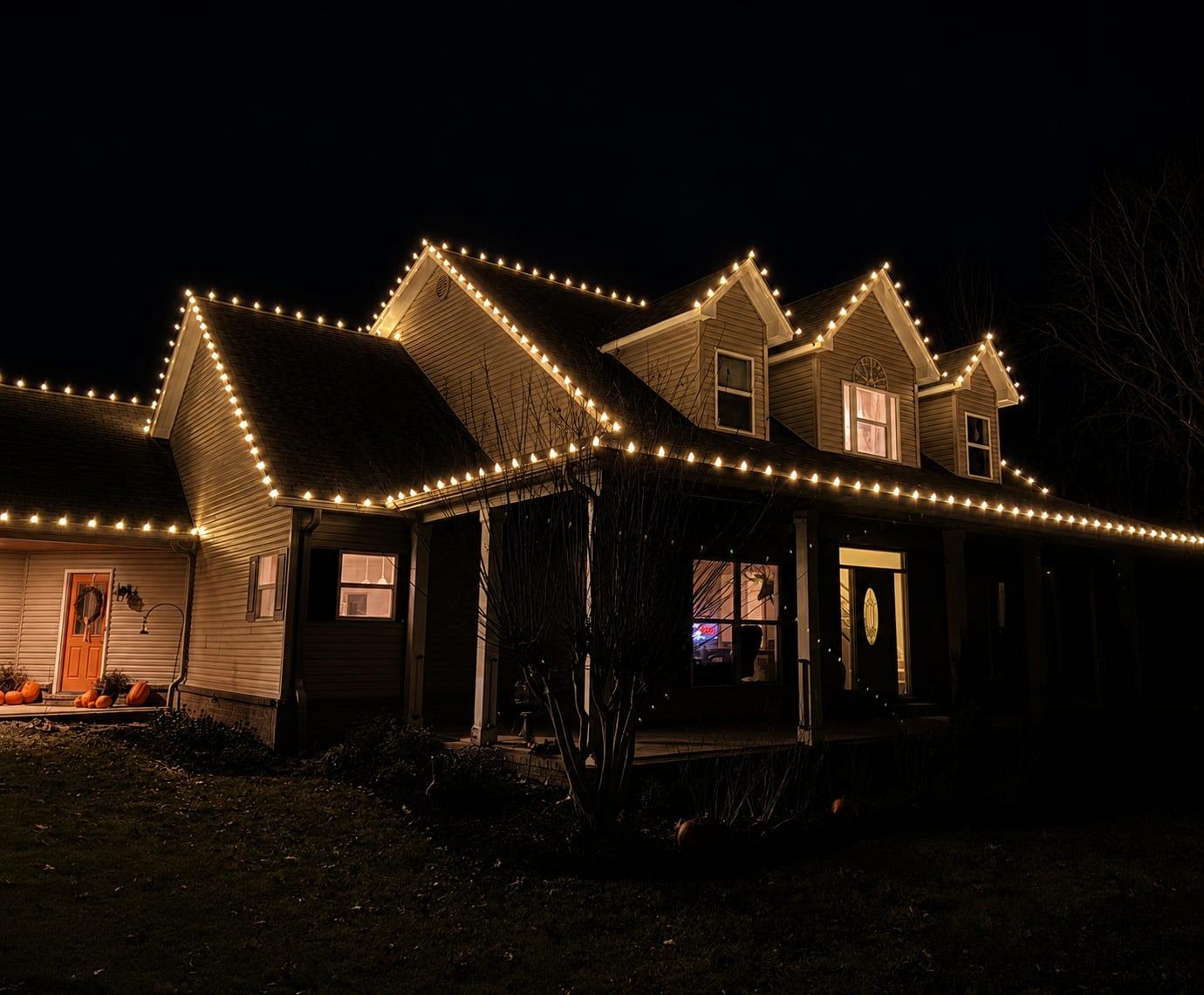 Two-story home with warm white C9 bulbs outlining three dormers and every roofline, beams of light visible against the night sky