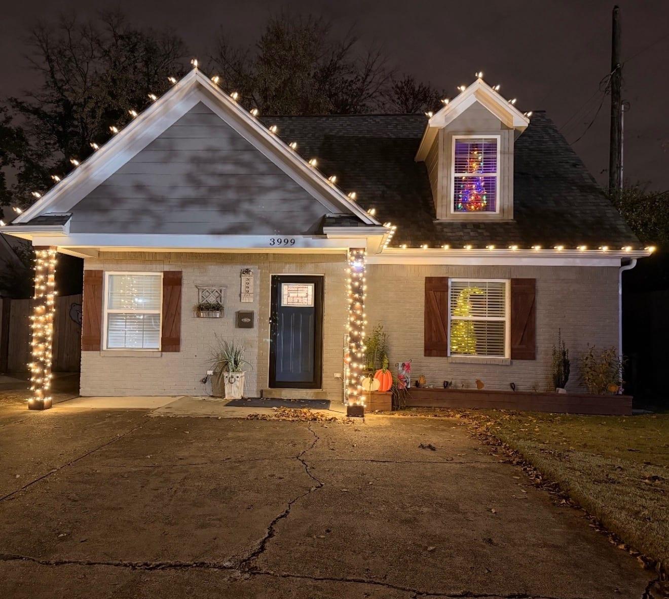 Cottage porch with both entry columns wrapped in warm white string lights and the roofline traced in C9 bulbs